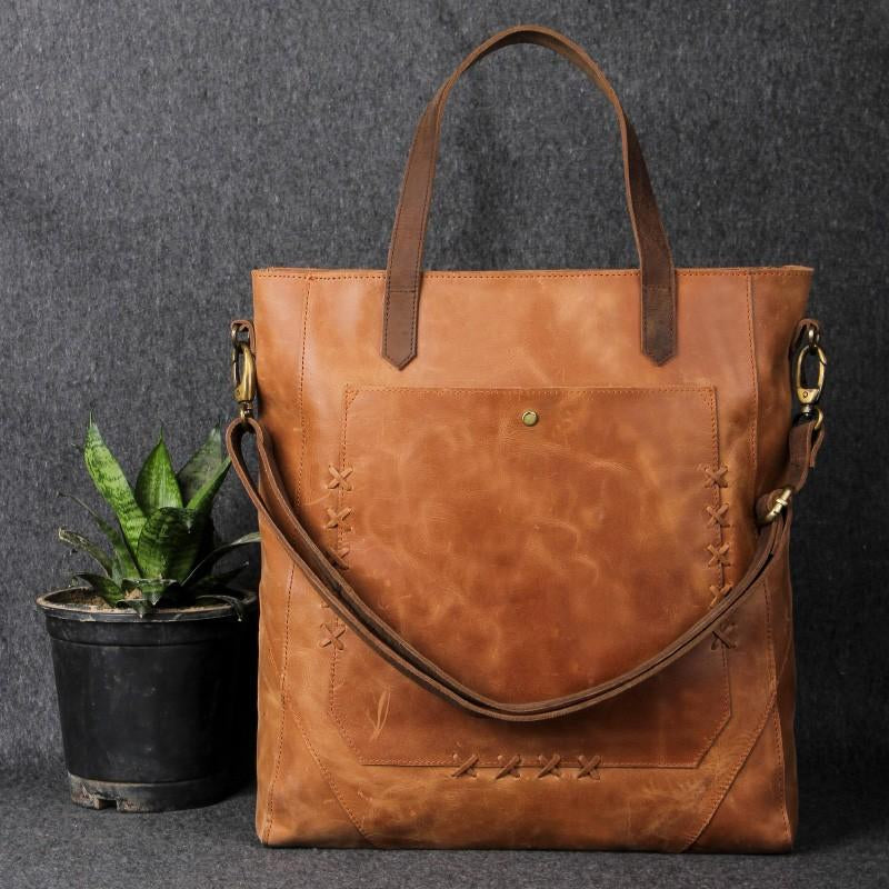 Brown leather tote bag with shoulder strap and front pocket placed on a studio background