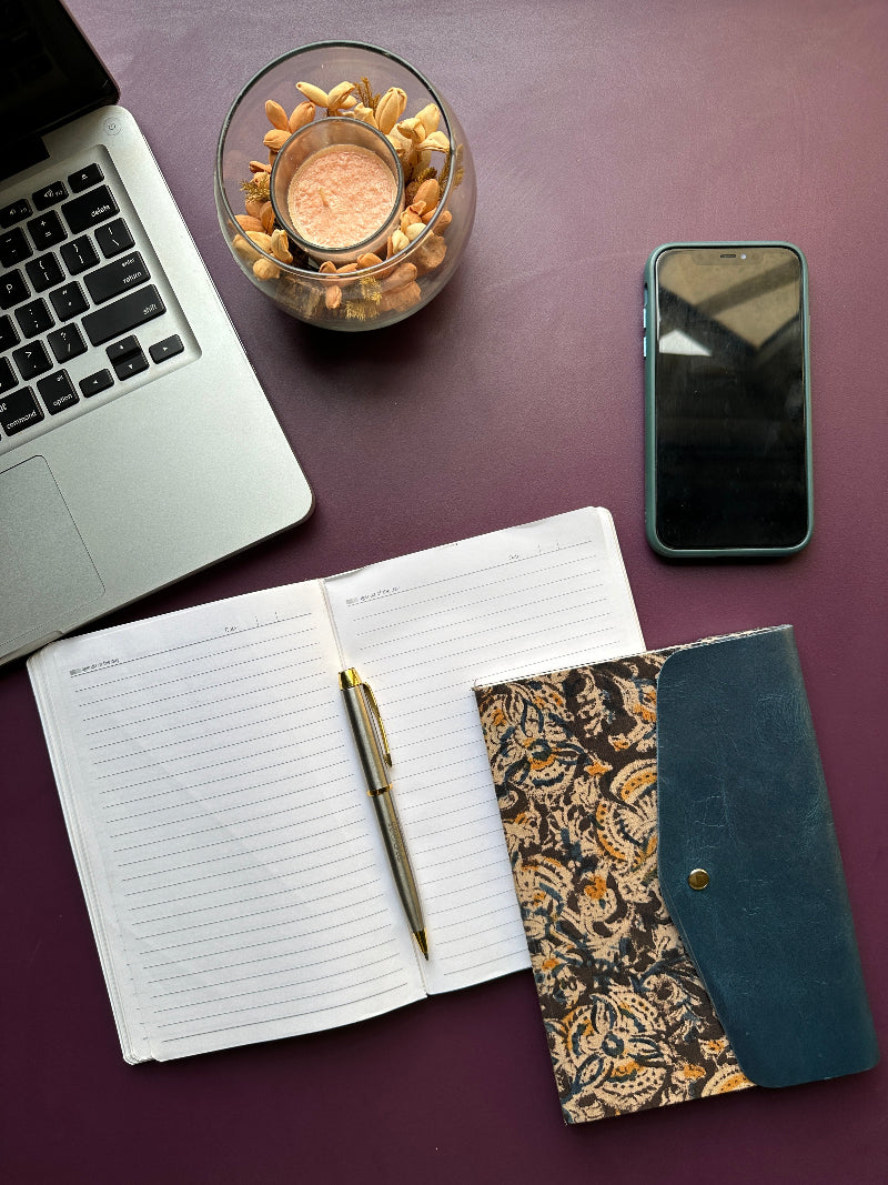 Laptop, notebook, pen, phone, and decorative items on a purple surface