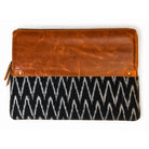 A rectangular clutch bag with a warm brown leather top half and a black and white ikat patterned bottom half, shown flat against a white background.