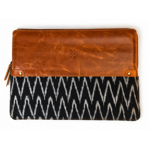 A rectangular clutch bag with a warm brown leather top half and a black and white ikat patterned bottom half, shown flat against a white background.