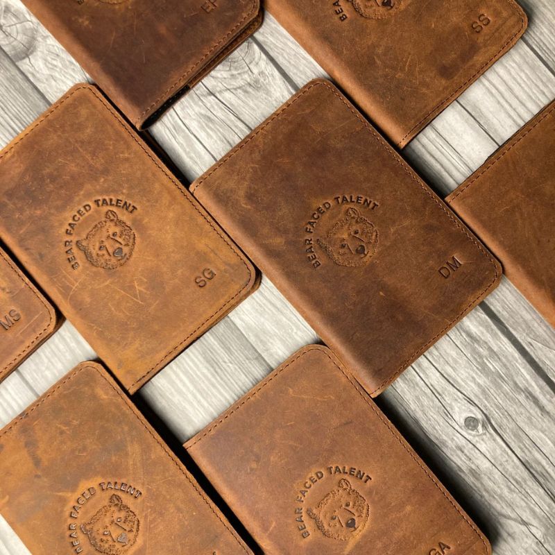 Brown leather passport covers with embossed logo on a wooden surface