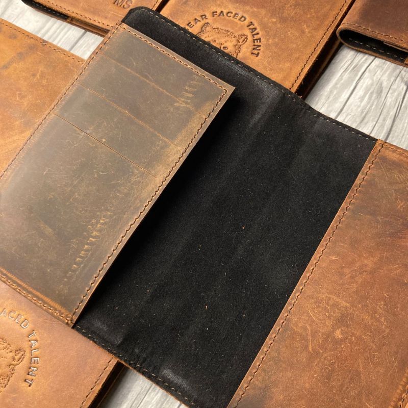 Close-up of brown leather passport cover with visible branding on a wooden surface.