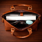 Brown leather briefcase with laptop and items on a wooden surface