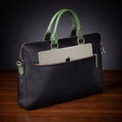 Black leather briefcase with green handles holding an Apple laptop on a wooden surface.