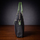 Black handbag with green handles and accents on a wooden surface with a dark background