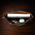 Open brown leather bag with electronic devices on a dark wooden surface