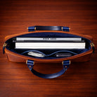 Brown leather briefcase with blue interior holding a laptop on a wooden surface