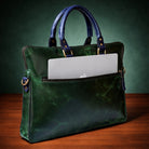 Green leather handbag with a laptop compartment on a wooden surface and green background