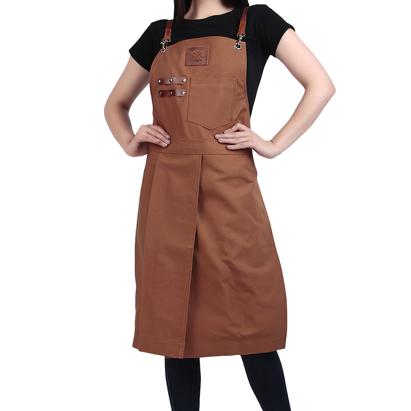 Brown full-length apron with leather strap details worn by a person in a black t-shirt, featuring a front pocket and metal hardware.