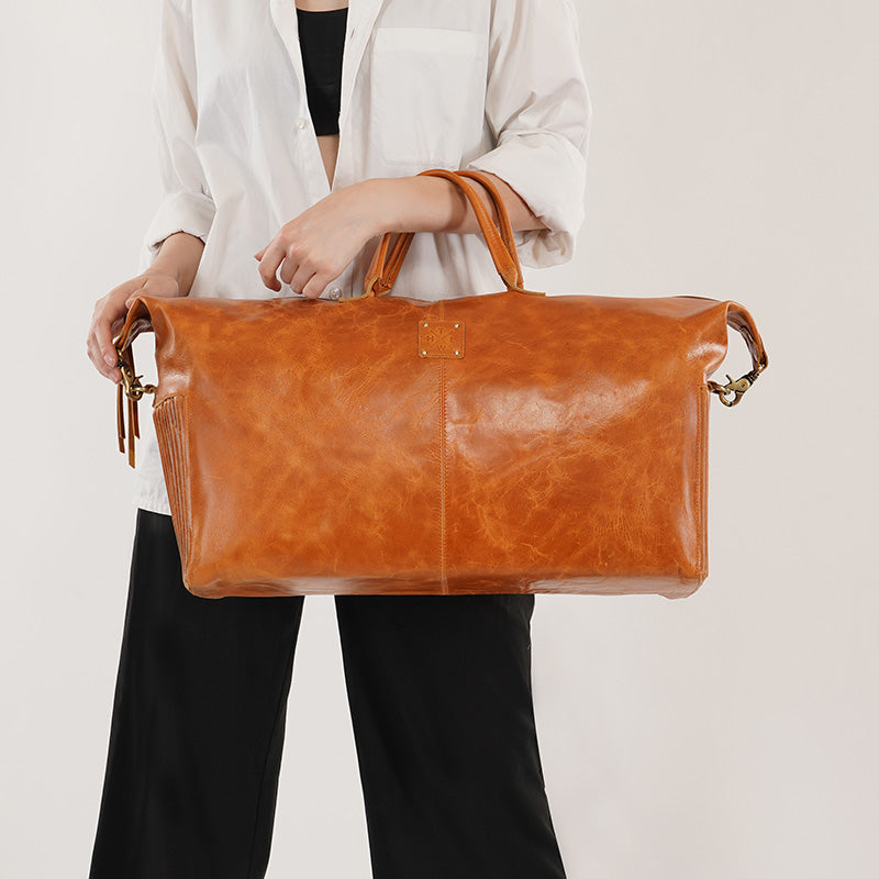 Brown leather travel duffle bag with top handles, carried by a woman, premium handcrafted leather weekender bag