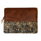 A rectangular zippered pouch or sleeve with a smooth brown leather top half and a dark patterned fabric bottom half featuring beige and gold floral motifs, shown on a white background.