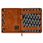 Open brown leather portfolio organizer with card slots, pen holders, document straps, and a black-and-white patterned interior.