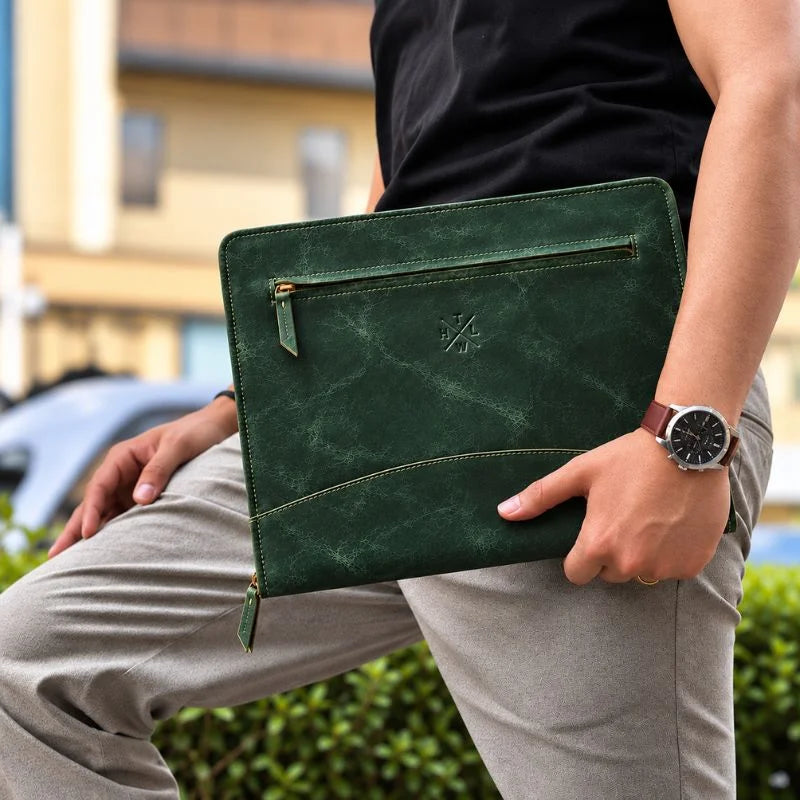 Man holding a green leather portfolio with a front zip pocket, contrast stitching, and an embossed logo.