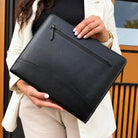 Open black leather portfolio showing a tablet in a snap-closure pocket, card slots, a pen, and gold-snap straps.
