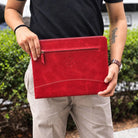 Man holding a red leather portfolio with a front zip pocket, light stitching, and an embossed logo.