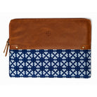 A zip-around pouch featuring a smooth brown leather top half and a navy blue fabric bottom half with a white geometric ikat pattern. The pouch has brass grommets, a leather zipper pull, and an embossed logo on the leather section.