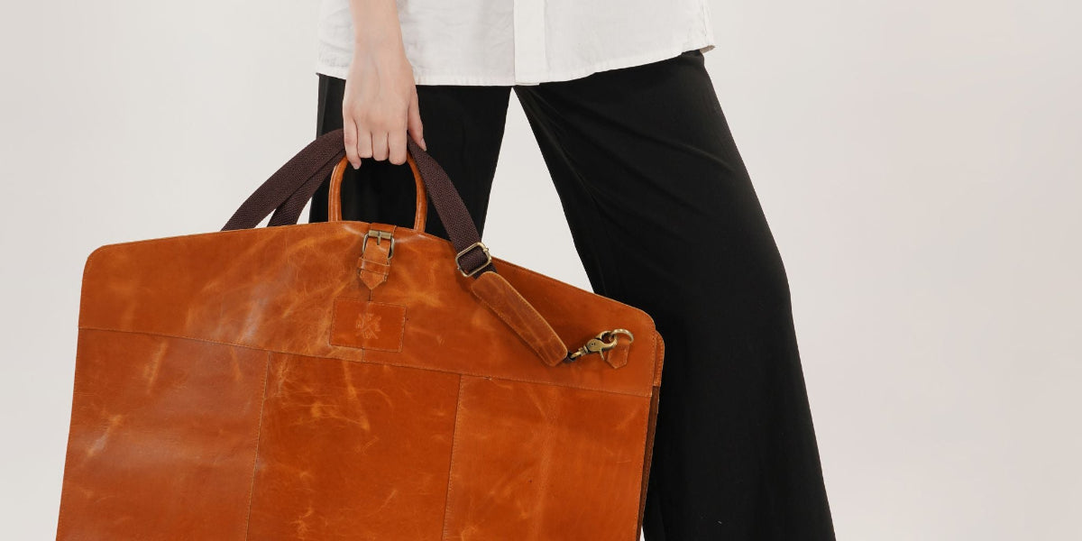 Person holding a brown leather briefcase against a plain background