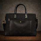 Black canvas & leather briefcase with gold accents on a wooden surface and dark background