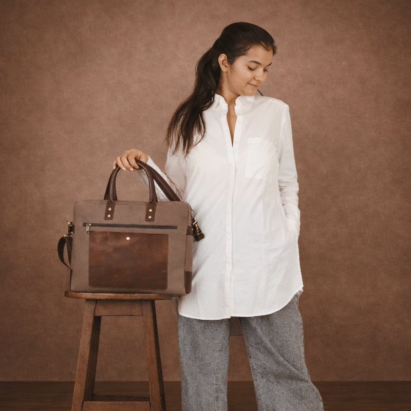 Woman holding a brown canvas  leather bag next to a wooden stool against a brown background