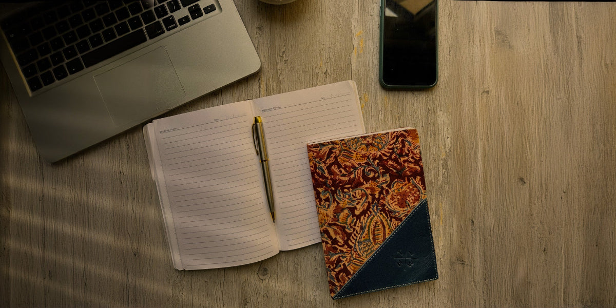 Open notebook with a pen, patterned notebook, and laptop on a wooden surface