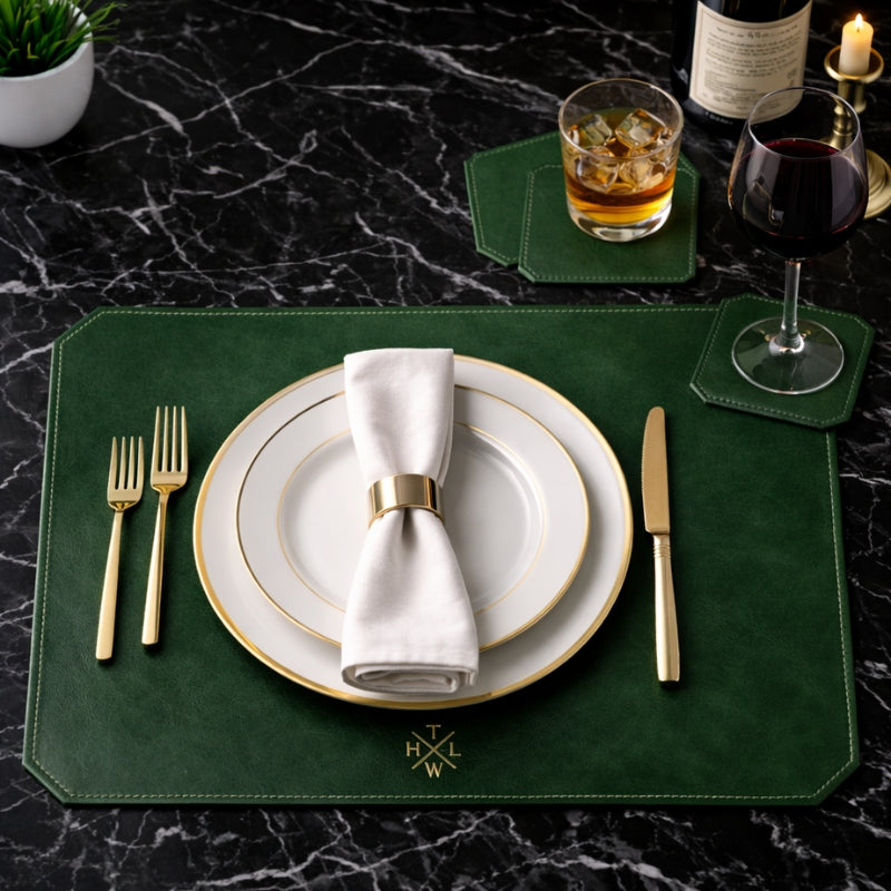 Dining table setting with green placemat and coaster white plates, gold cutlery, and glasses on a dark marble surface.