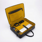 Open black briefcase with yellow interior containing a laptop, notebook, and other items on a white background