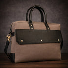 Brown canvas and black leather handbag with gold accents on a dark background