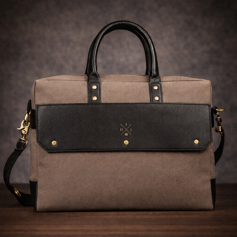 Brown canvas and black handbag with gold accents on a wooden surface and dark background