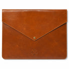 A brown leather envelope-style pouch with a flap closure and a small metal snap button, shown on a plain white background. An embossed monogram is visible near the bottom center.