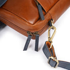Close-up of a Tan leather bag with a gold clasp and blue strap on a white background
