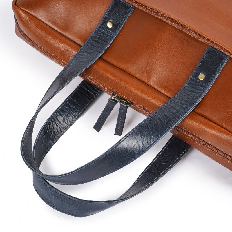 Tan leather bag with a blue strap on a white background