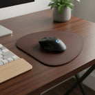 Black gaming mouse on a brown mouse pad with a plant and keyboard in the background