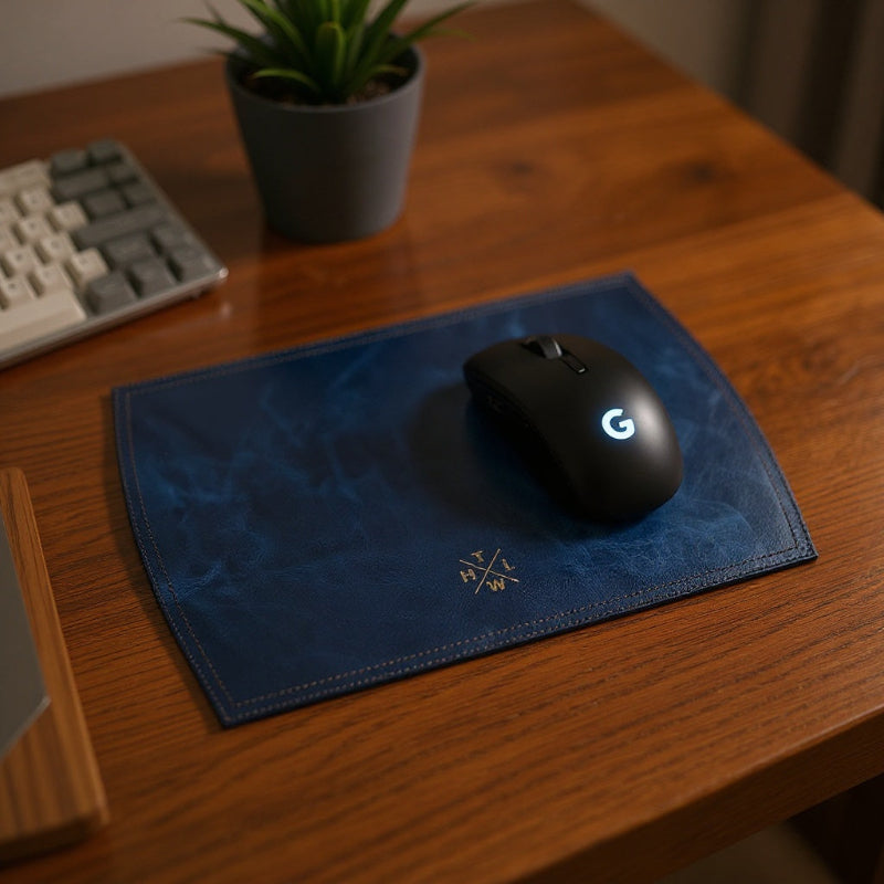 Black gaming mouse with a logo on a blue mouse pad on a wooden desk.
