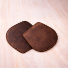Two brown leather coasters on a light wooden surface