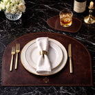 Dining table setting with plates, cutlery, and a monogrammed placemat and coaster on a dark marble surface.