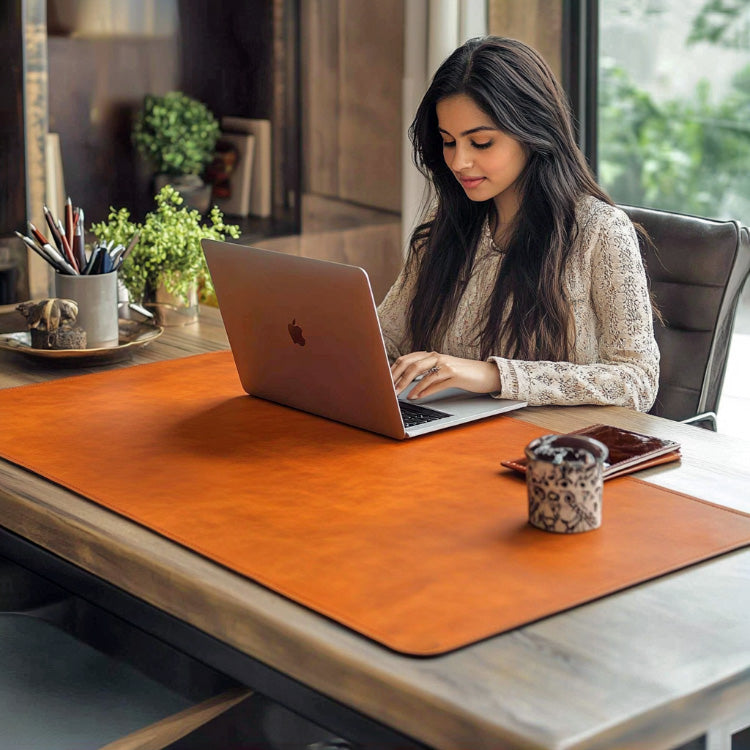 A woman working on a laptop at a wooden desk with a large brown leather desk mat, surrounded by office accessories in a modern workspace.